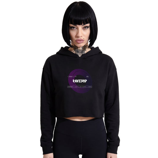 Front-facing studio product shot of a female model with a black bob haircut wearing a RAVEDRIP black cropped hoodie with tucked-in drawstrings. Features a vibrant purple techwear vortex circle graphic on the chest with the RAVEDRIP logo. Paired with high-waisted tight black leggings on a pure white background. Premium e-commerce streetwear photography.