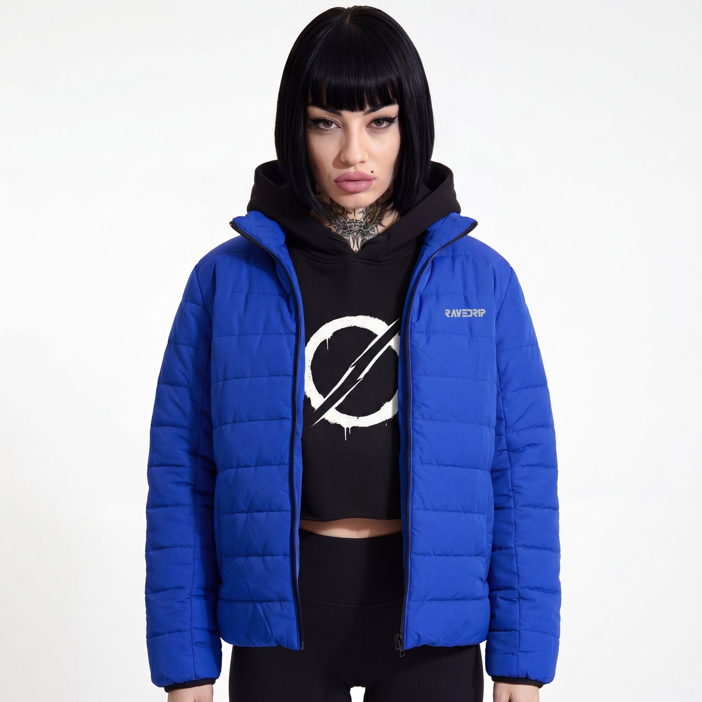 Front view of a model wearing the RAVEDRIP Cobalt Blue Light Puffer Jacket, styled open over a black crop hoodie with an industrial white graphic against a solid white studio background.