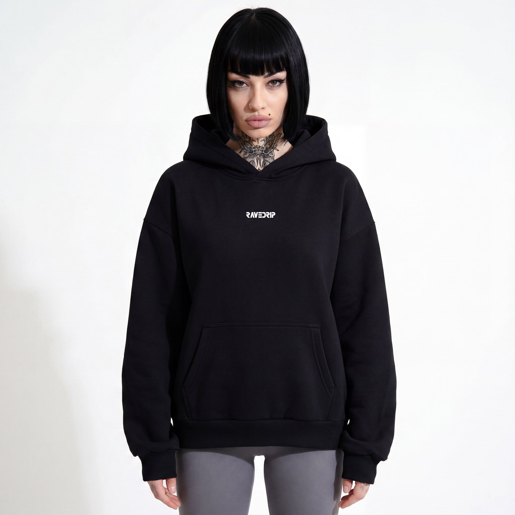 Front view of a woman wearing the RAVEDRIP Blank Slate Heavyweight Hoodie in matte black, showcasing the clean drawstring-less hood design, dropped shoulders, and centered black logo.