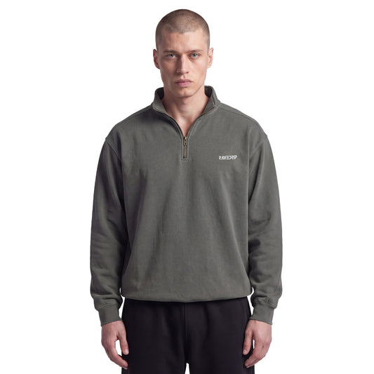 Male model with an edgy aesthetic styling the RAVEDRIP Sector 210 heavyweight quarter-zip sweatshirt in pepper charcoal with black sweatpants on a white studio background.