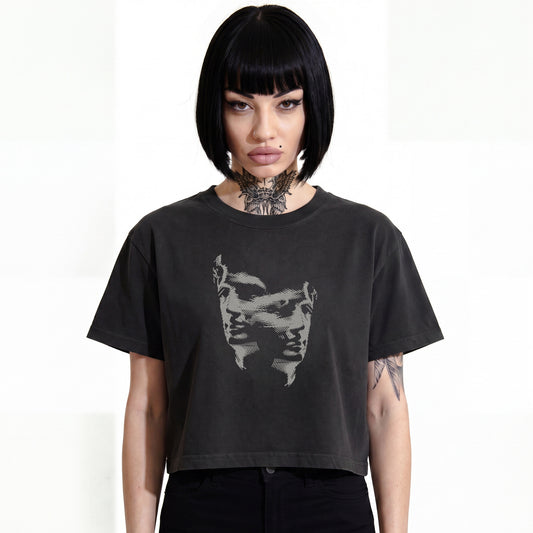 RAVEDRIP Duality heavyweight boxy cropped tee in faded black, premium wide square fit women's streetwear t-shirt with a grey engraved Janus-style double face duality graphic print on the chest, worn by alternative female model with a black bob haircut and neck tattoo, professional e-commerce studio catalog photography on a white background.