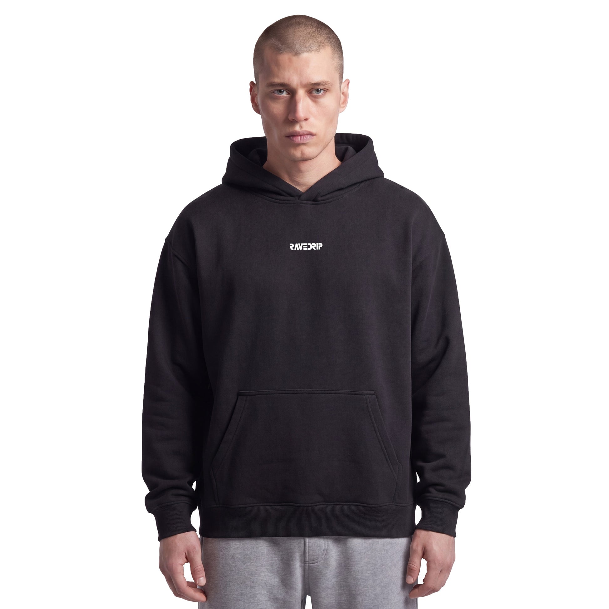 Studio lookbook portrait of male model wearing the RAVEDRIP Core Relaxed heavyweight hoodie in Black. The 9.4oz AS Colour fleece hoodie features a drawstring-less double-layer hood, dropped shoulders, and a small minimalist white logo printed on the high chest, styled for an edgy, iconic streetwear look.
